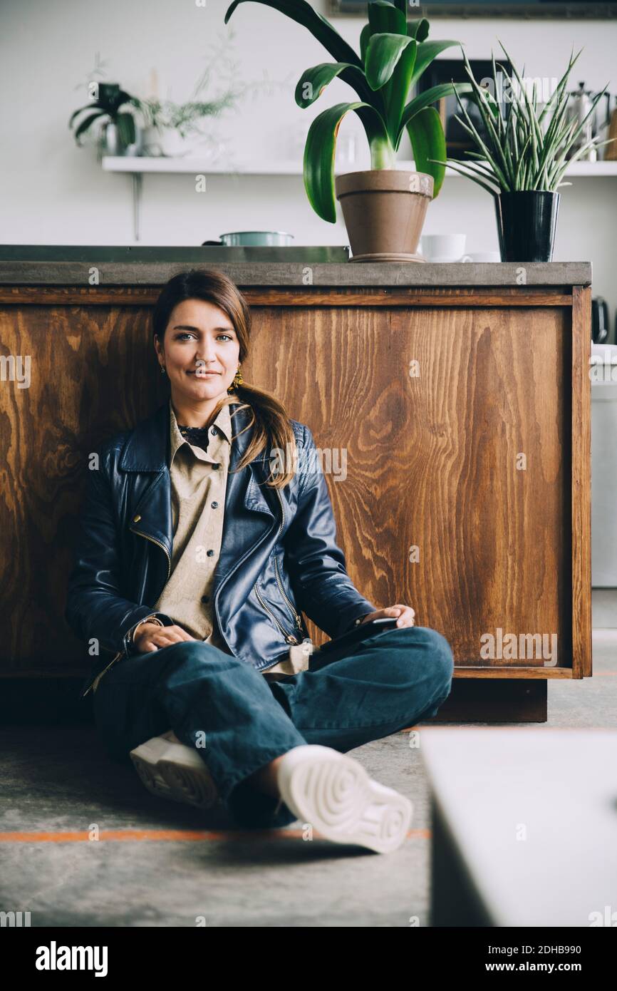 Full length portrait of creative businesswoman sitting against kitchen island in office Stock Photo