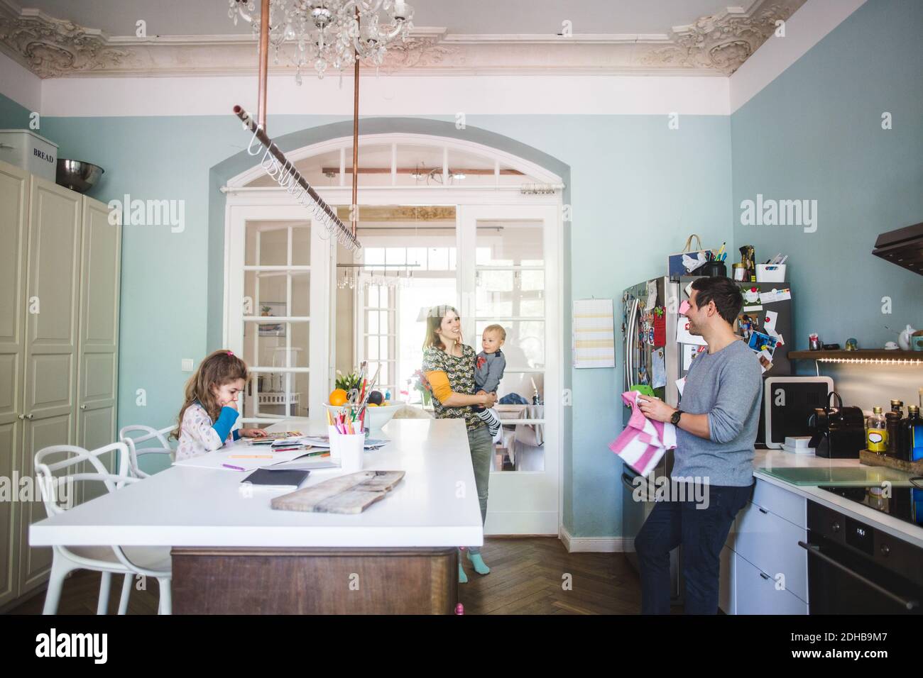 Smiling woman carrying son while talking to man standing in kitchen at home Stock Photo