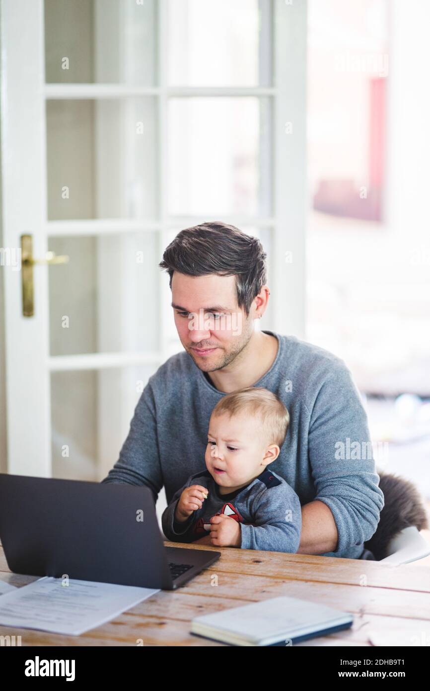 Man working on laptop while sitting with son at table Stock Photo