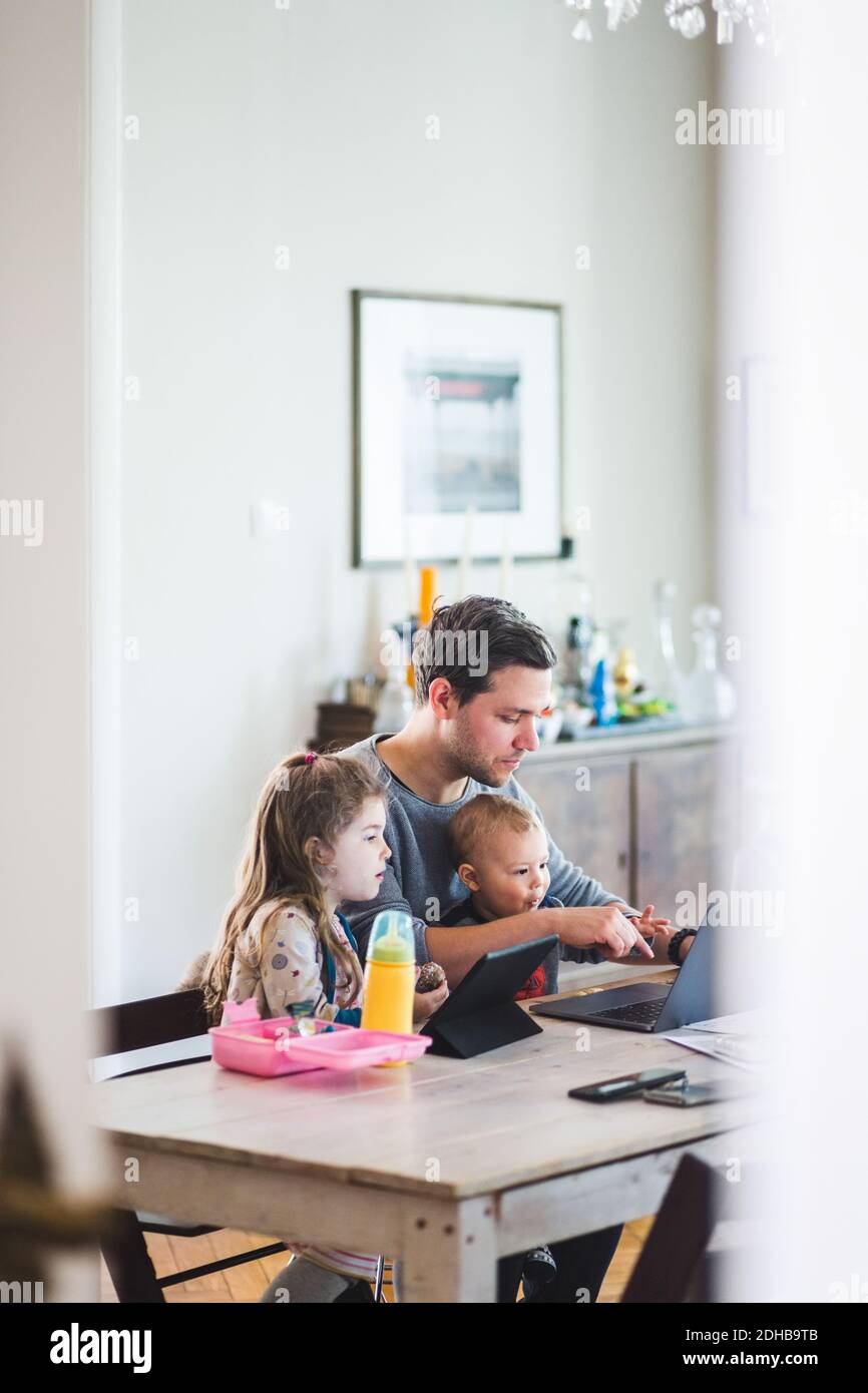 Father using laptop while sitting with cute children at table Stock Photo