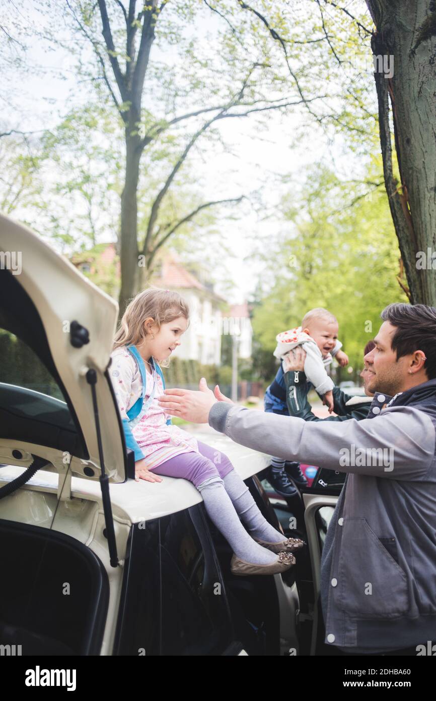 Father gesturing towards girl sitting on car Stock Photo