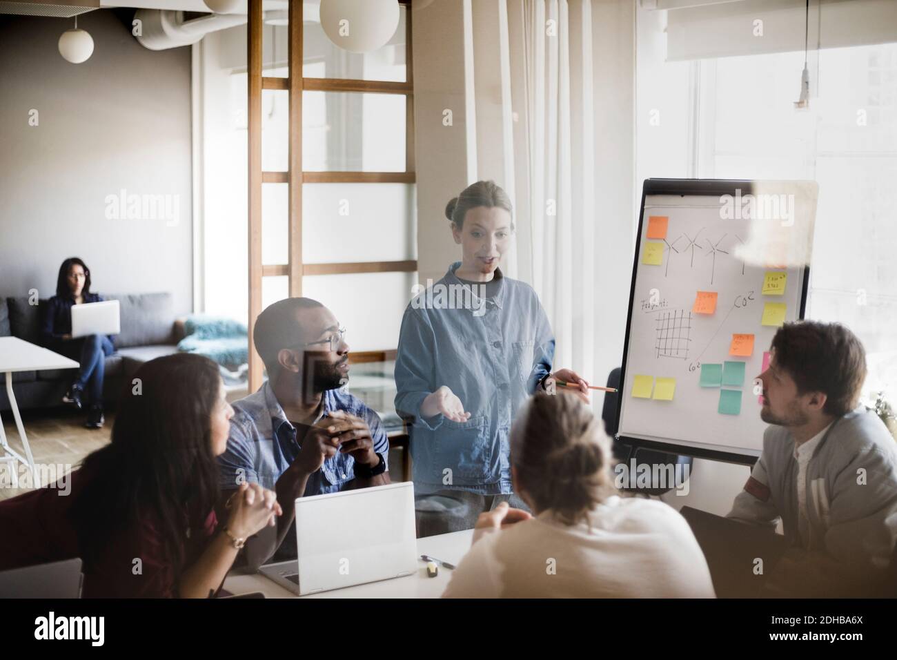 Businesswoman explaining business plan to colleagues in board room seen through glass wall Stock Photo