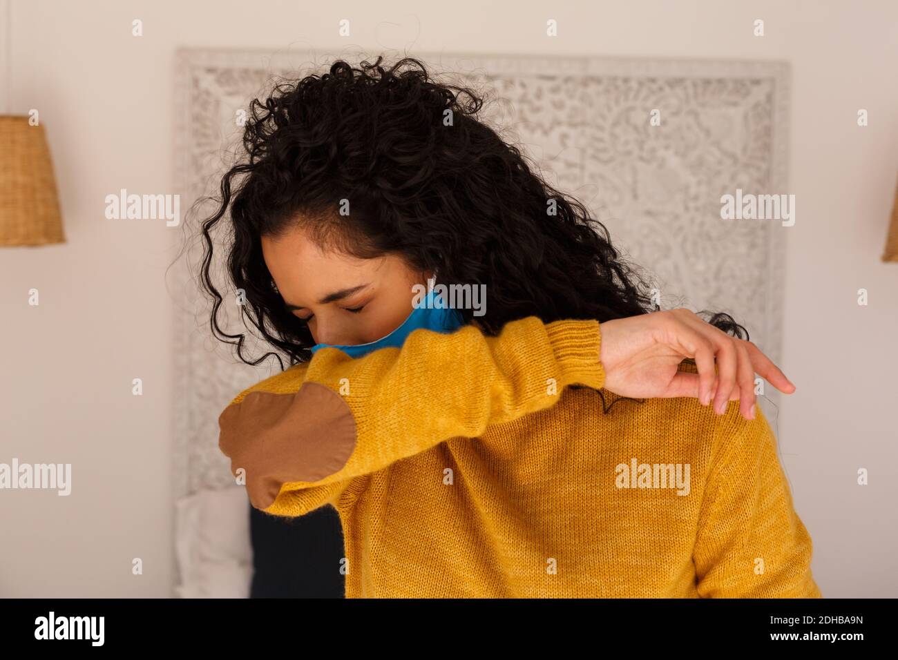 Mixed race woman wearing face mask coughing into arm Stock Photo