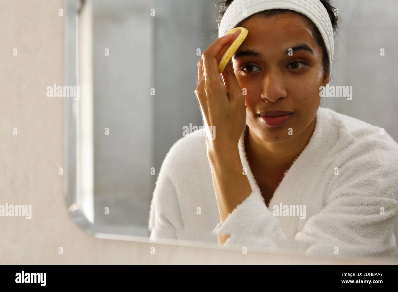 Mixed race woman reflected in mirror cleansing face in bathroom Stock Photo