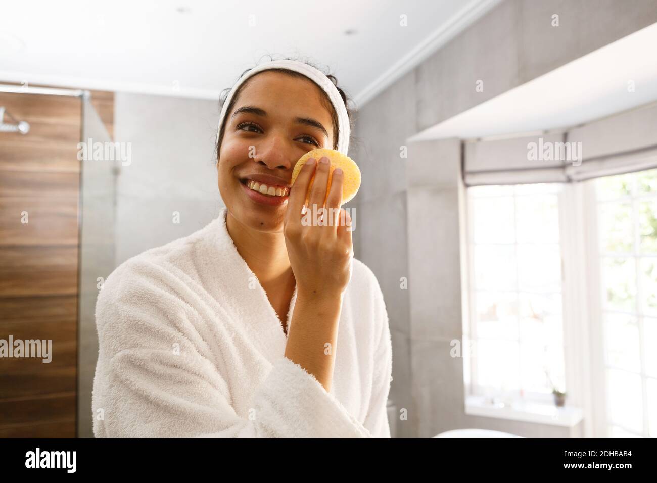 Mixed race woman looking in mirror cleansing face in bathroom Stock Photo