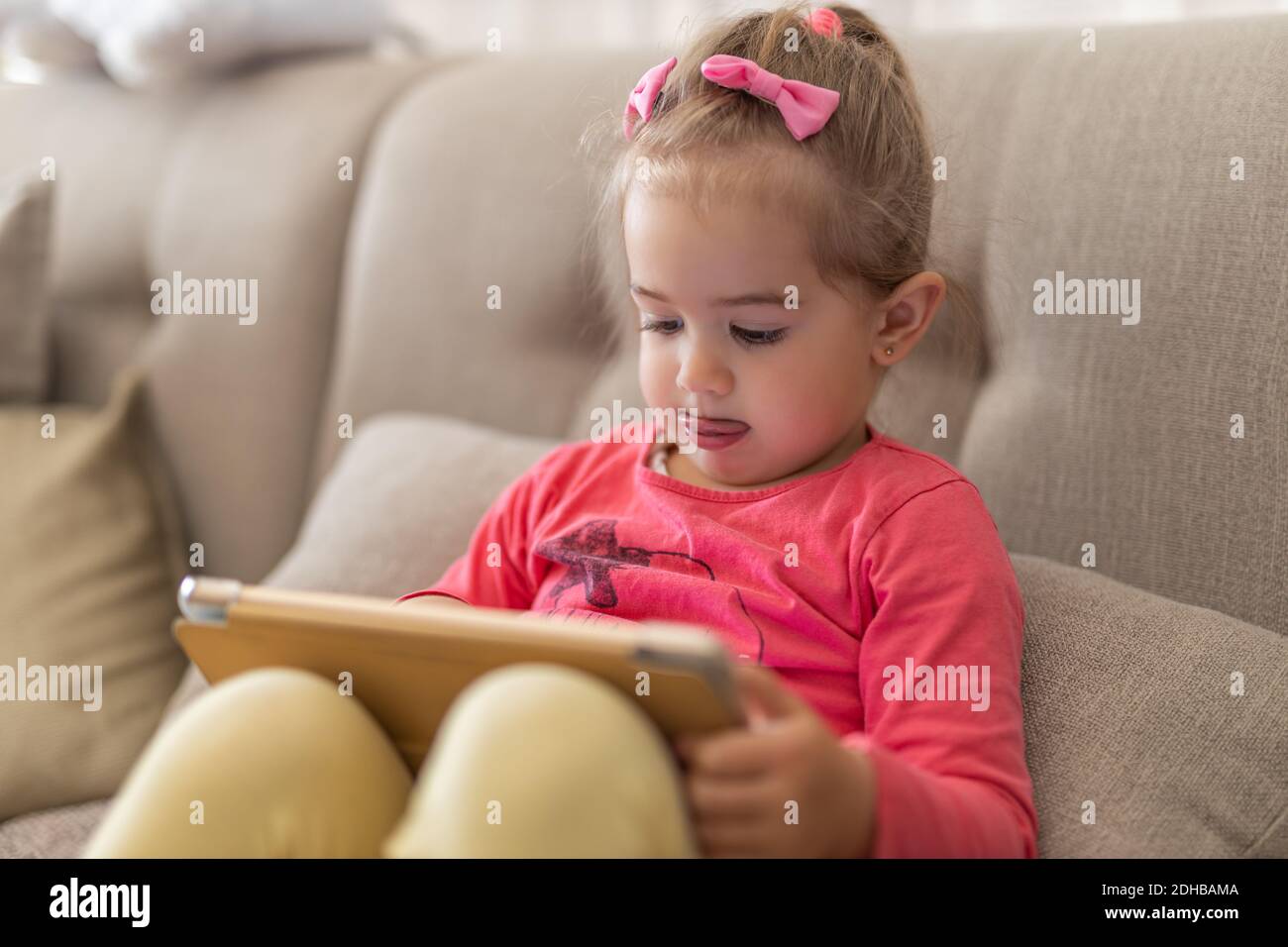 Young cute girl sitting at home using a child's tablet touch screen computer during home schooling due to closure of schools and pre-schools. Toddler Stock Photo