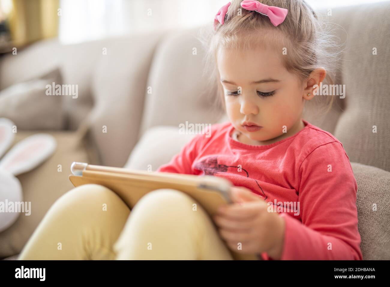 Young cute girl sitting at home using a child's tablet touch screen computer during home schooling due to closure of schools and pre-schools. Toddler Stock Photo