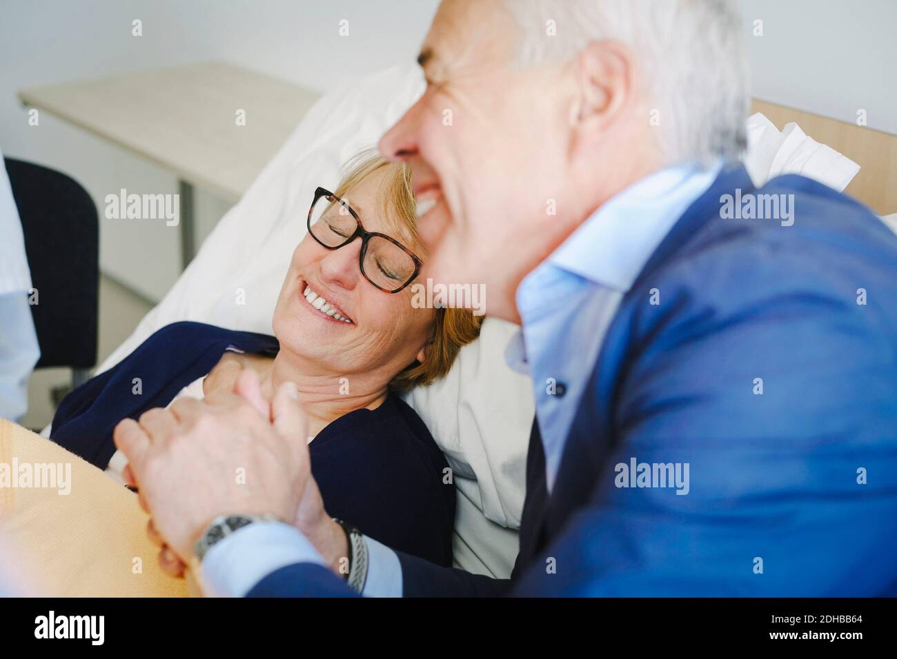 Smiling woman with eyes closed by senior partner in hospital ward Stock Photo
