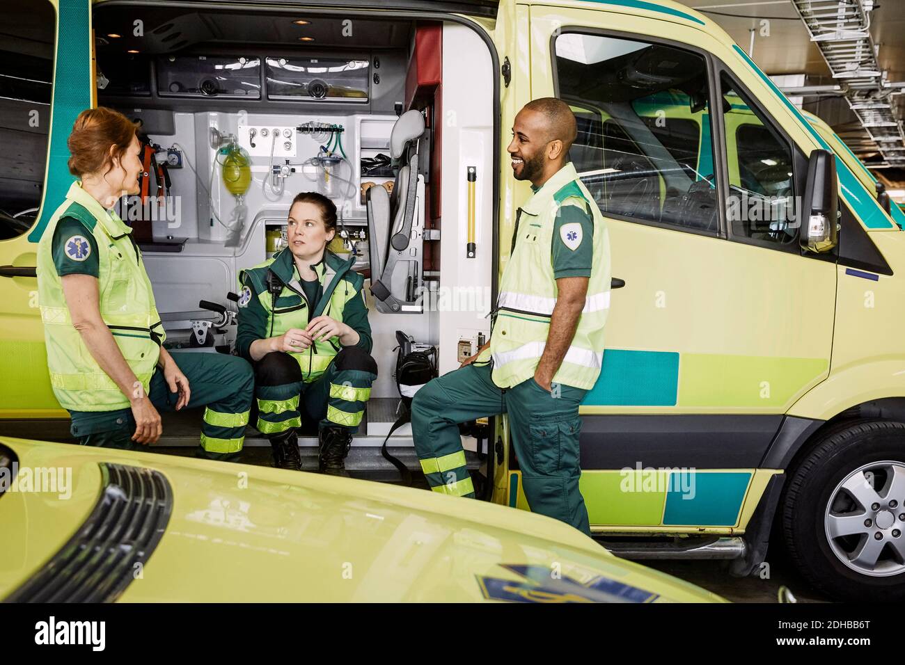 Male and female paramedics talking while sitting in ambulance at parking lot Stock Photo