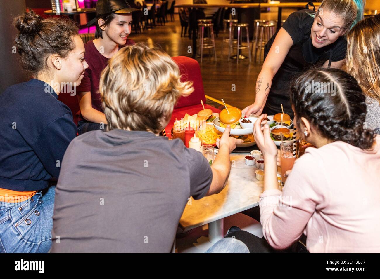 Smiling waitress serving food to multi-ethnic teenagers sitting at restaurant Stock Photo
