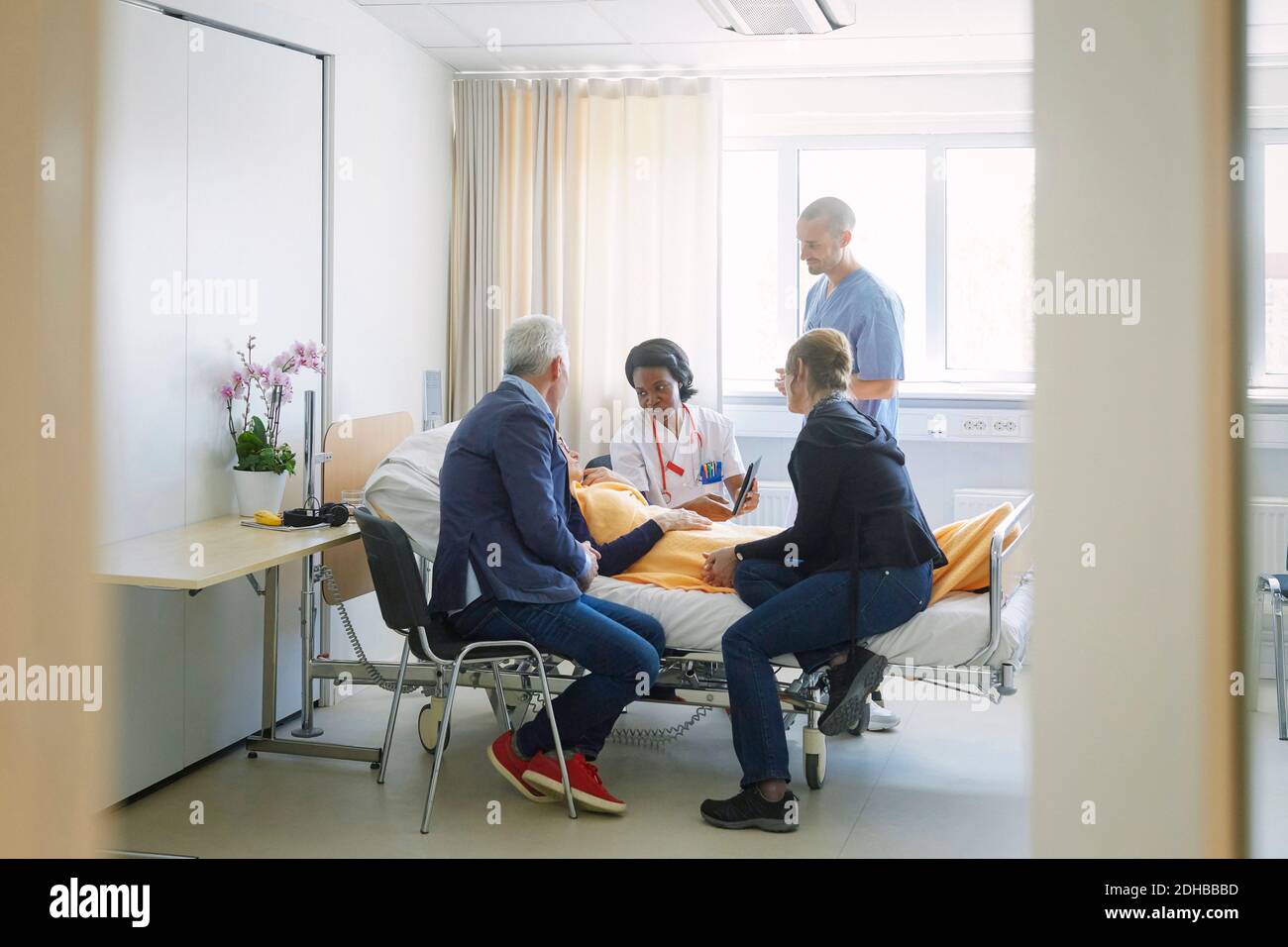 Medical professionals discussing with patient and her friends in ward at hospital Stock Photo