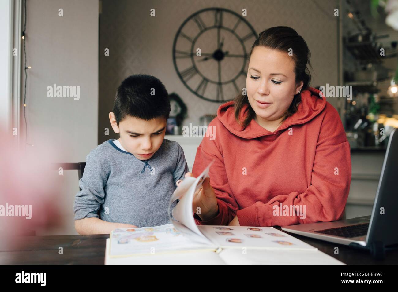 Mother reading story from picture book for autistic son while sitting at home Stock Photo