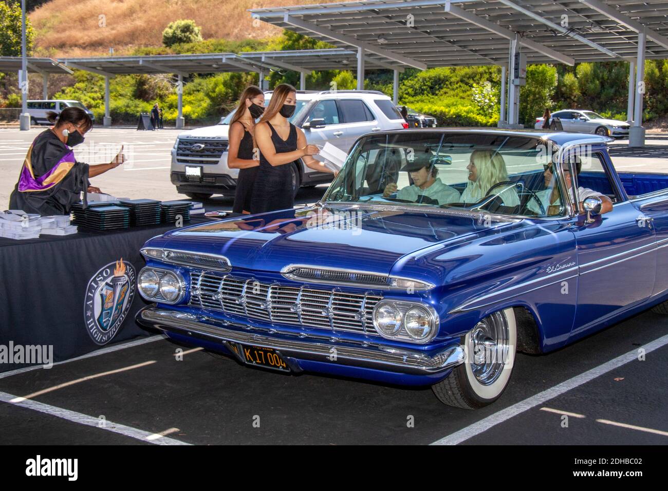 Wearing face masks due to the coronavirus pandemic, student assistants give a diploma to a graduating senior in a 1959 Chevrolet El Camino during driv Stock Photo
