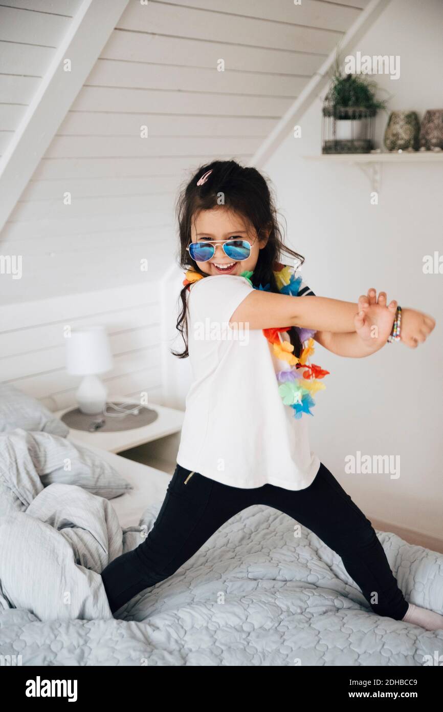 Portrait of happy girl wearing sunglasses dancing on bed at home Stock