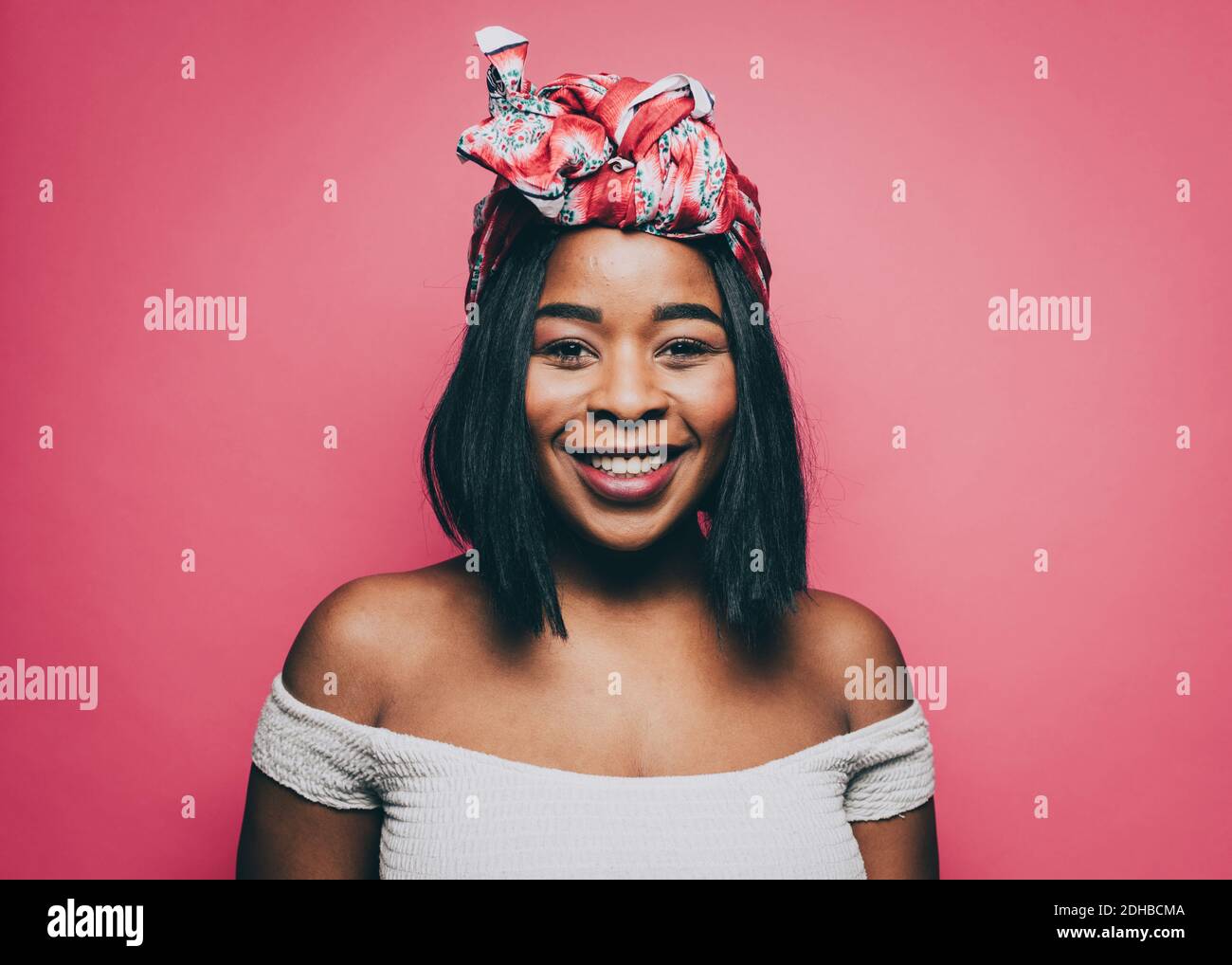 Portrait of smiling woman wearing head tie over pink background Stock Photo