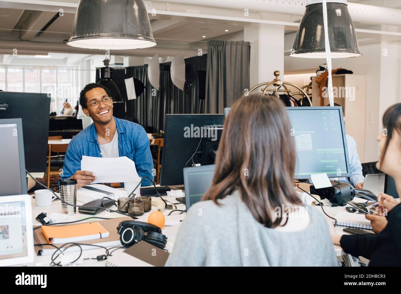 Cheerful multi-ethnic IT professionals talking while sitting at desk in creative office Stock Photo