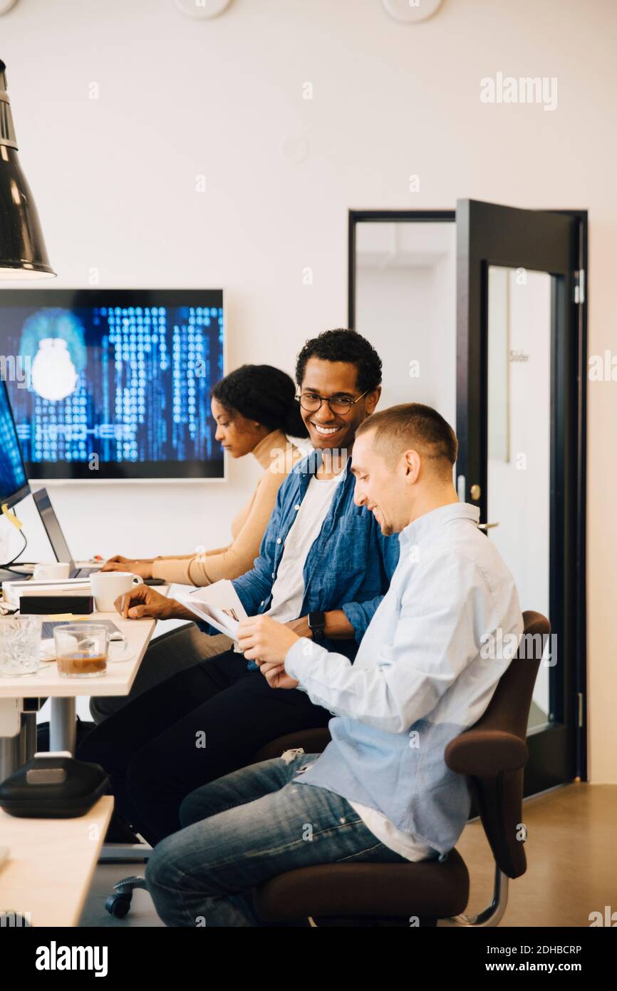 Male programmers discussing while female working in background at creative office Stock Photo