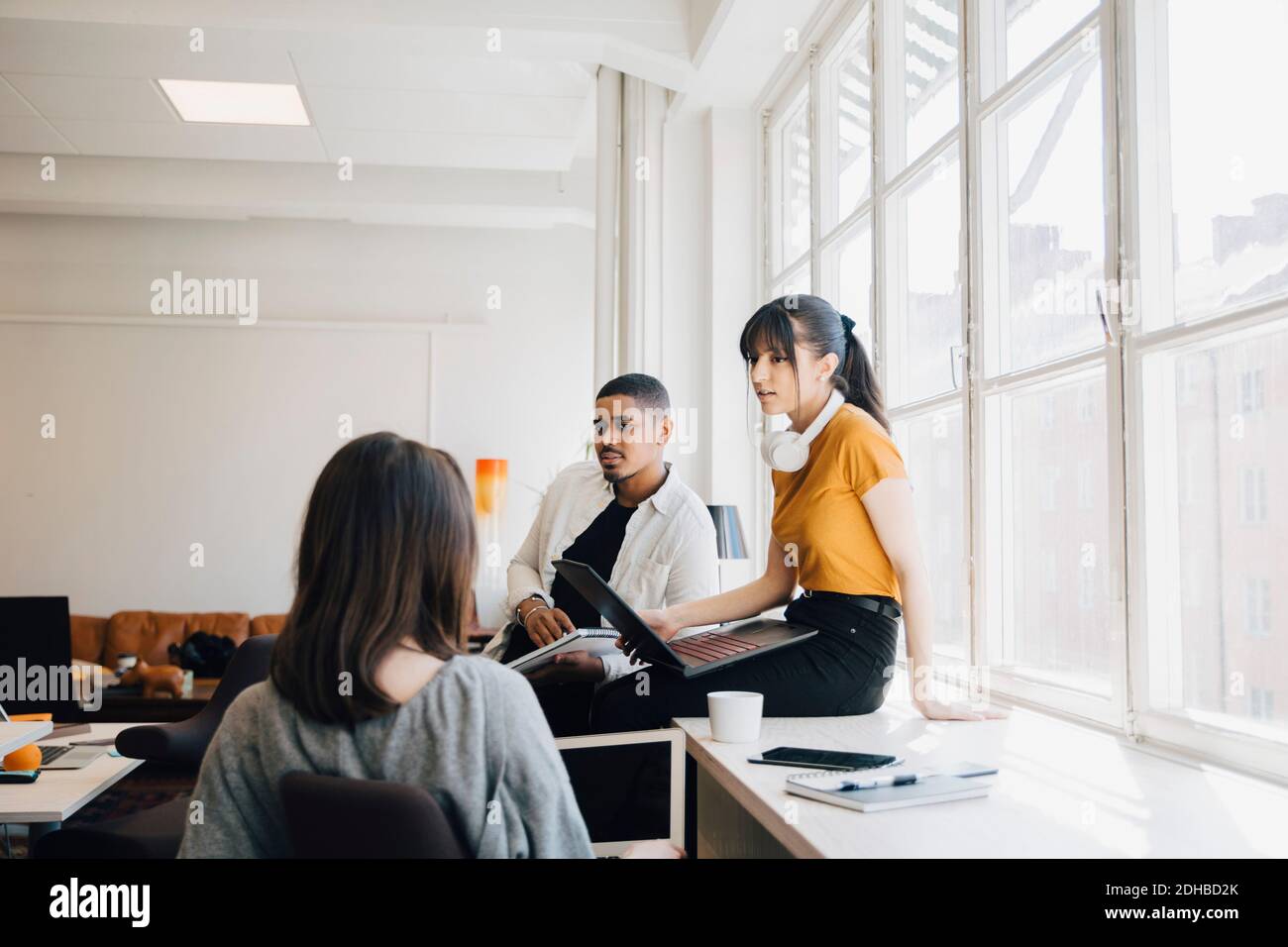 Female computer engineer discussing with colleagues while sitting on desk in office Stock Photo