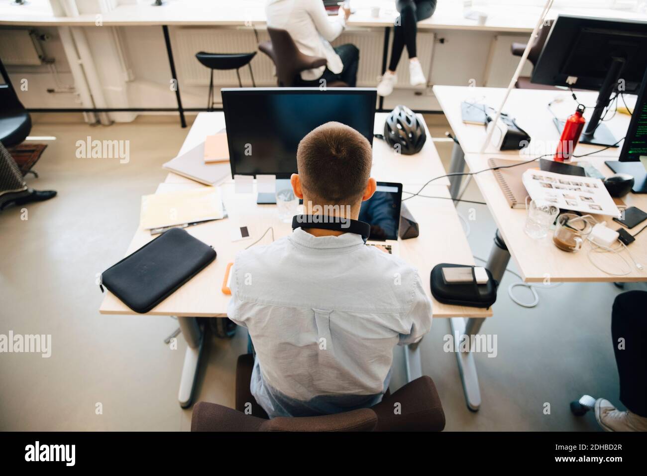 Rear view of male computer programmer using laptop on desk while ...