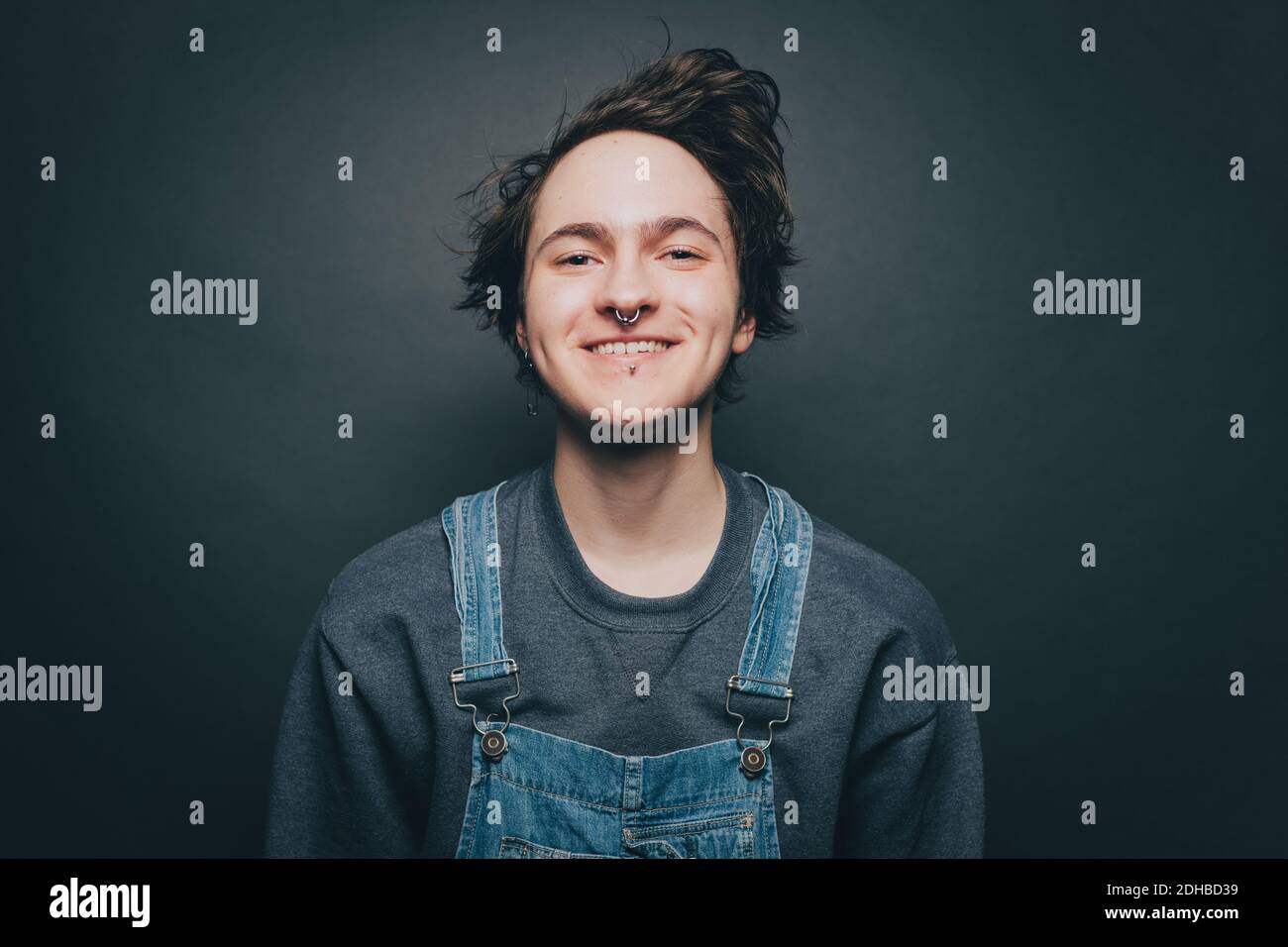 Portrait of smiling young man wearing denim overalls over gray background Stock Photo