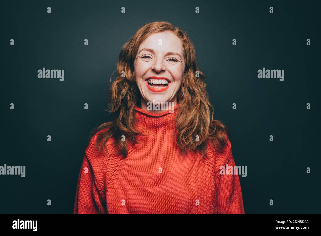 Portrait of woman in orange top laughing against gray background Stock Photo