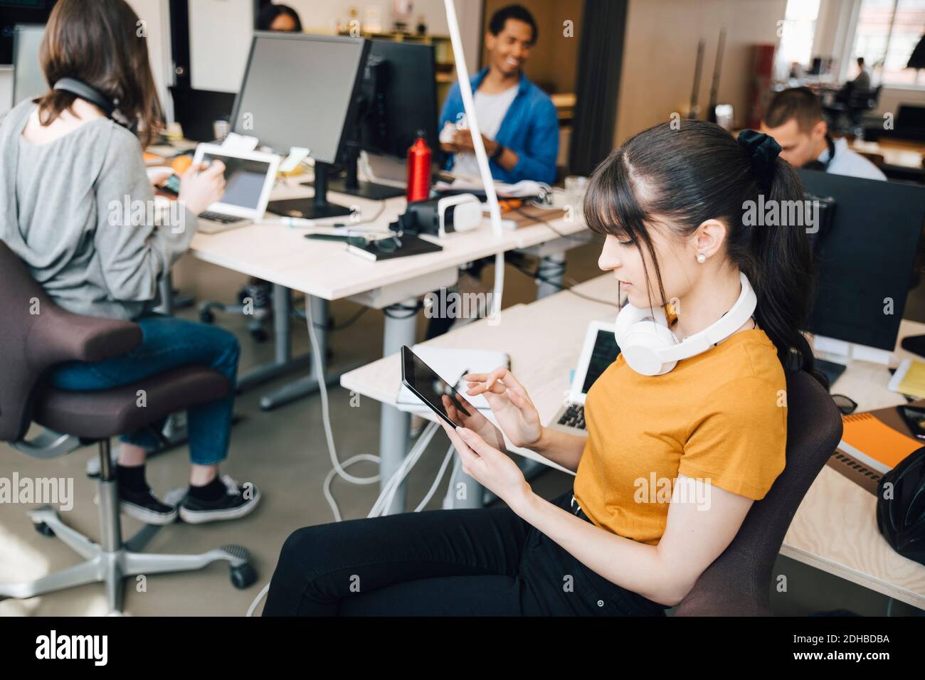 Female IT computer hacker using digital tablet while coworkers working in creative office Stock Photo