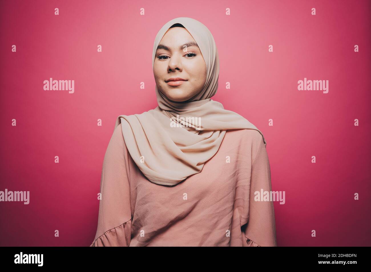 Portrait of confident young woman wearing hijab against pink background ...