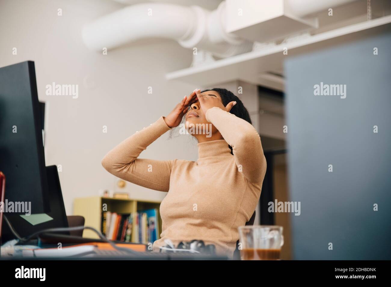 Frustrated female computer programmer with head in hands sitting in creative office Stock Photo