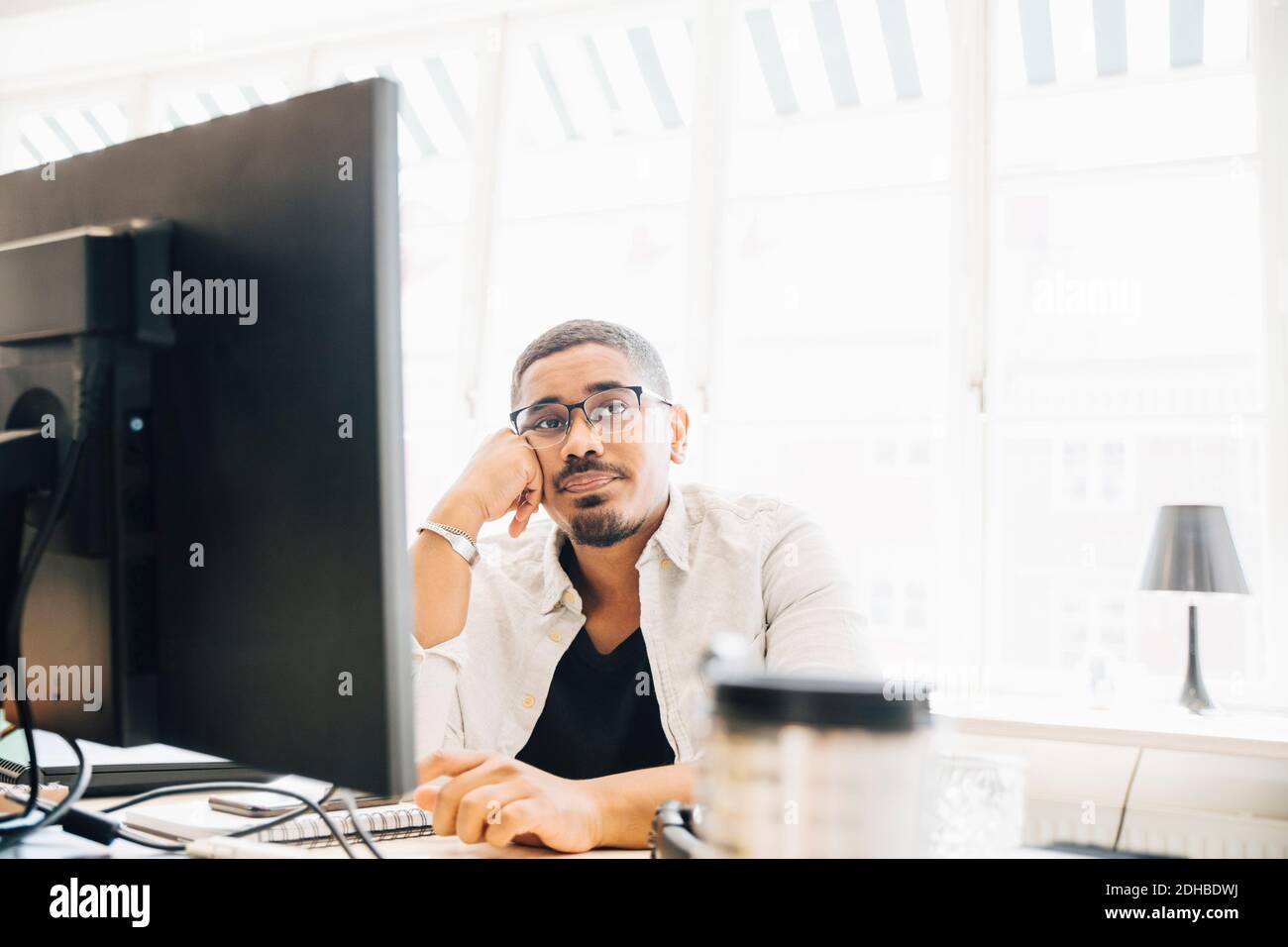 Thoughtful computer programmer looking away while sitting by window in office Stock Photo