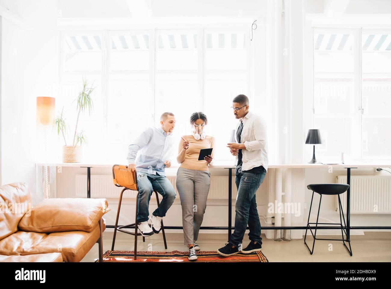 Full length of computer programmers looking at digital tablet while discussing by window in office Stock Photo