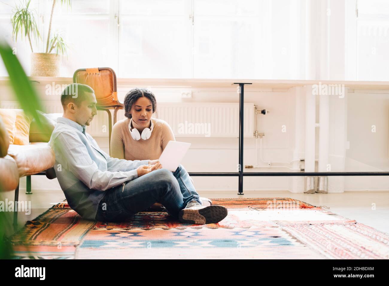 Programmers working over laptop while sitting on carpet in office Stock Photo