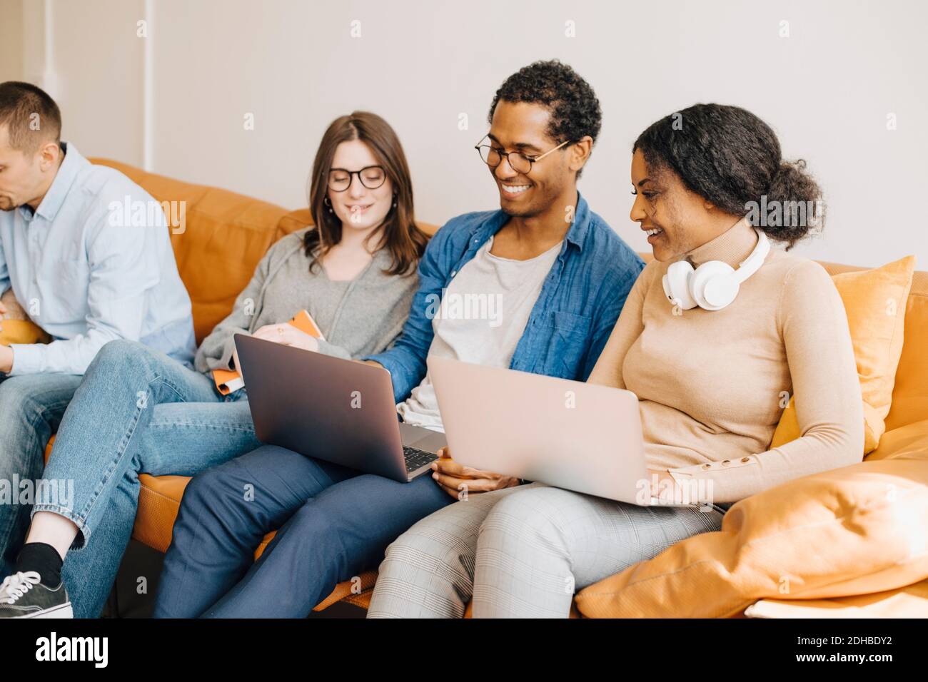 Smiling programmers working over laptops while sitting on sofa in creative office Stock Photo