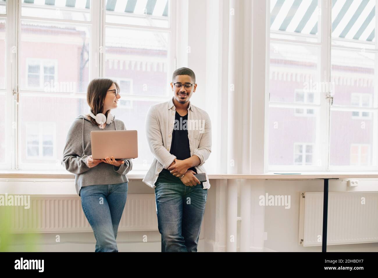 Smiling computer programmers talking while standing by desk in office ...
