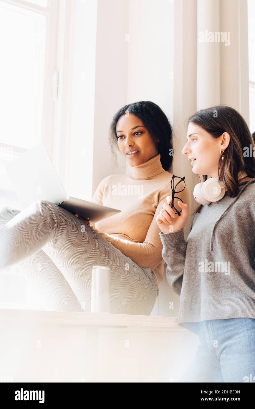 Female computer programmers discussing over laptop by window in office Stock Photo