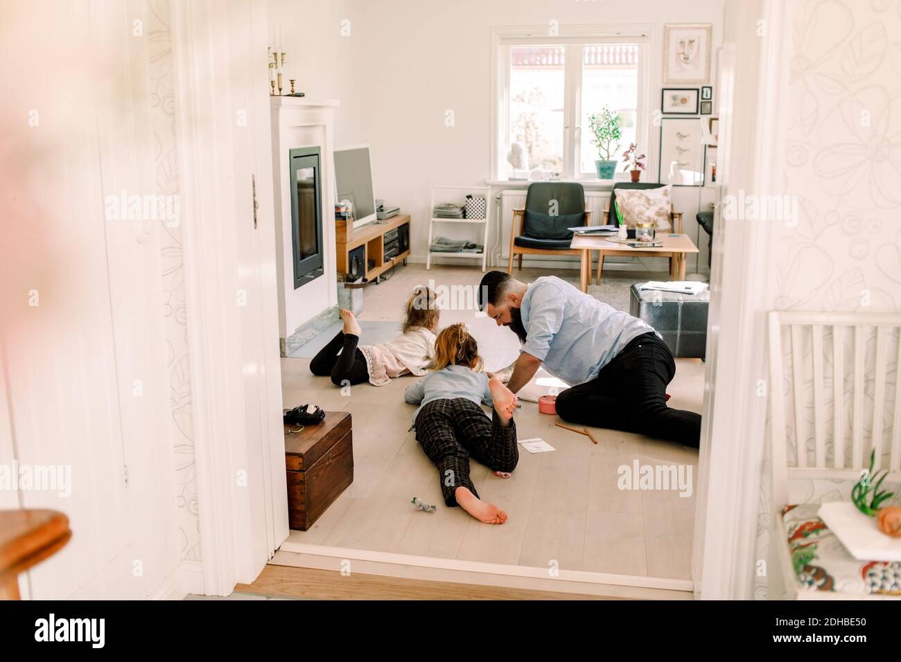 Mid adult man drawing with daughters while resting in living room at home Stock Photo