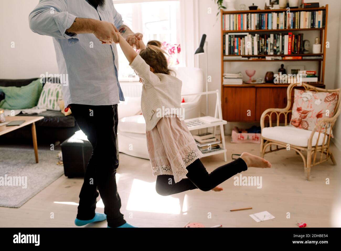 Father swinging playful girl while standing in living room at home Stock Photo