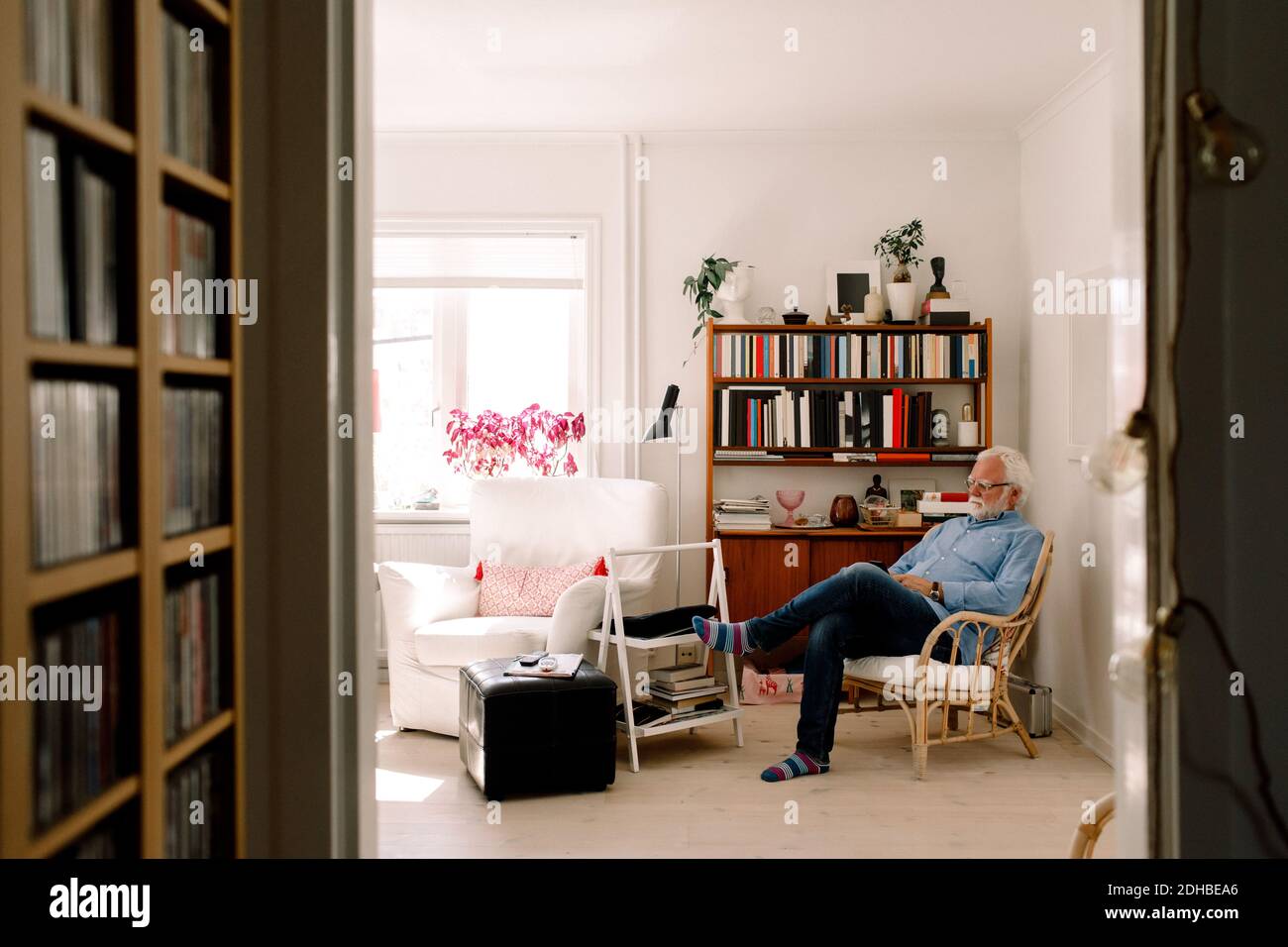 Full length of senior man sitting on chair in living room seen from doorway Stock Photo