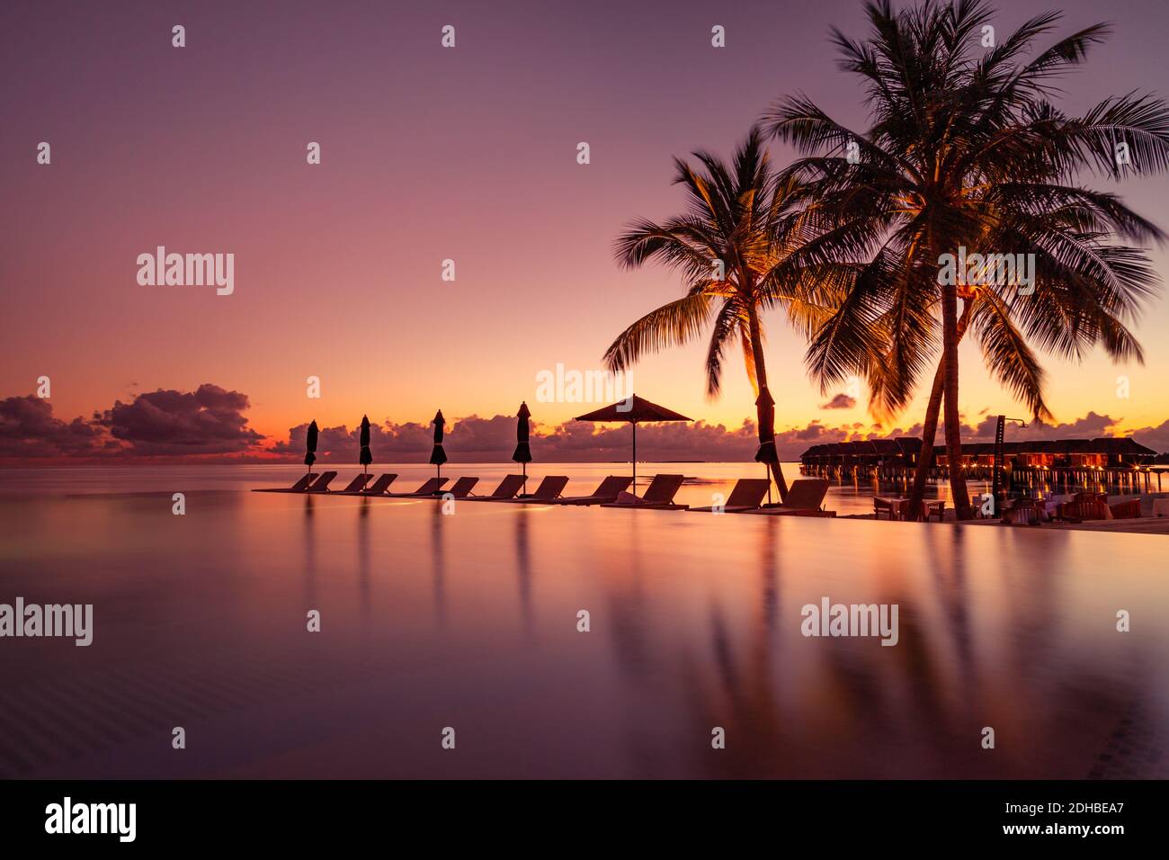 Beautiful poolside and sunset sky. Luxurious tropical beach landscape, deck chairs and loungers and water reflection. luxury swimming pool on beach Stock Photo