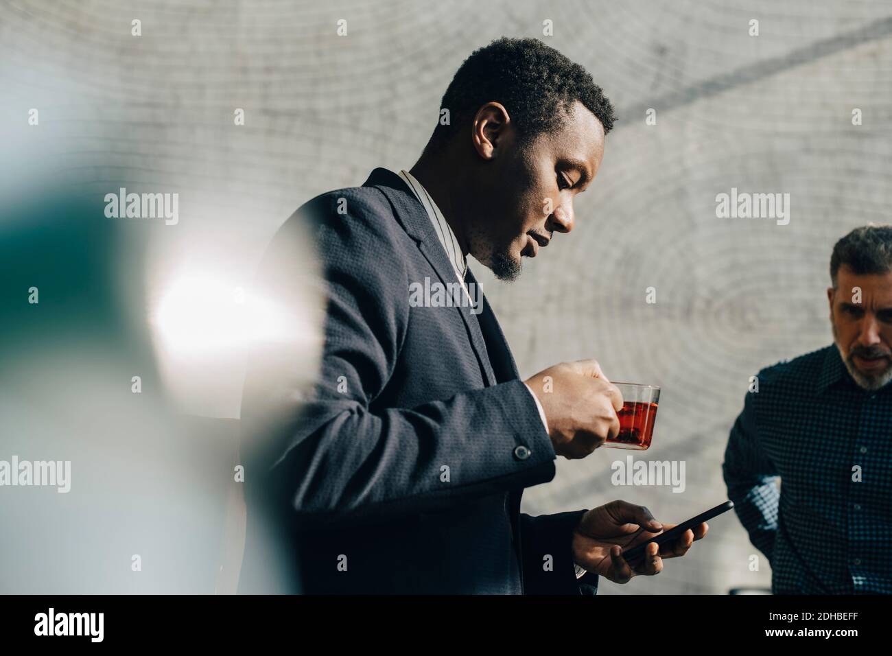 Young businessman using mobile phone while having tea at office Stock Photo