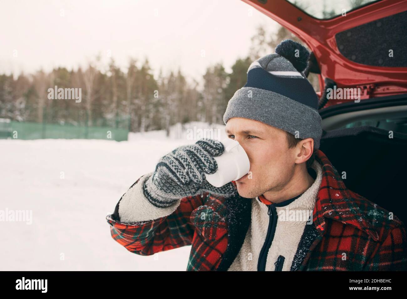 Man drinking coffee in car trunk at park during winter Stock Photo