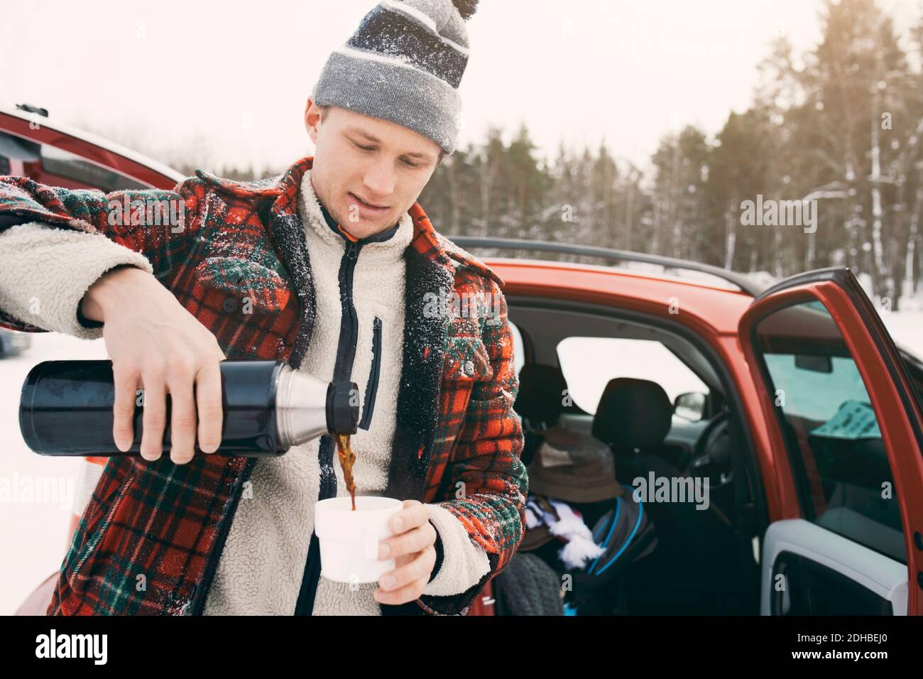 Mid adult man pouring coffee from insulated drink container while standing by car Stock Photo