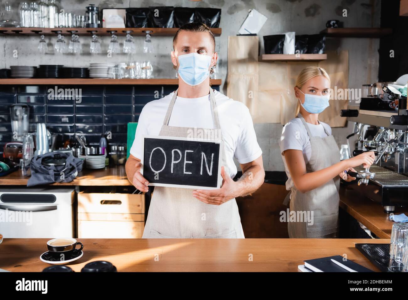 Waiter Lettering waiter in medical mask holding board with open lettering near barista ...
