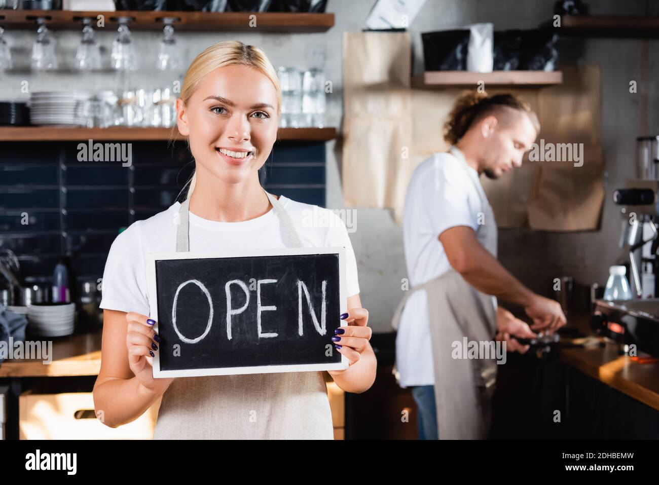 Waiter Lettering young smiling waiter holding board with open lettering near barista ...