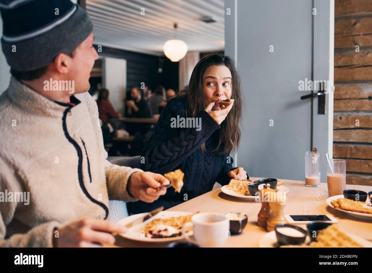 Woman eating breakfast while sitting with friend at table in log cabin Stock Photo