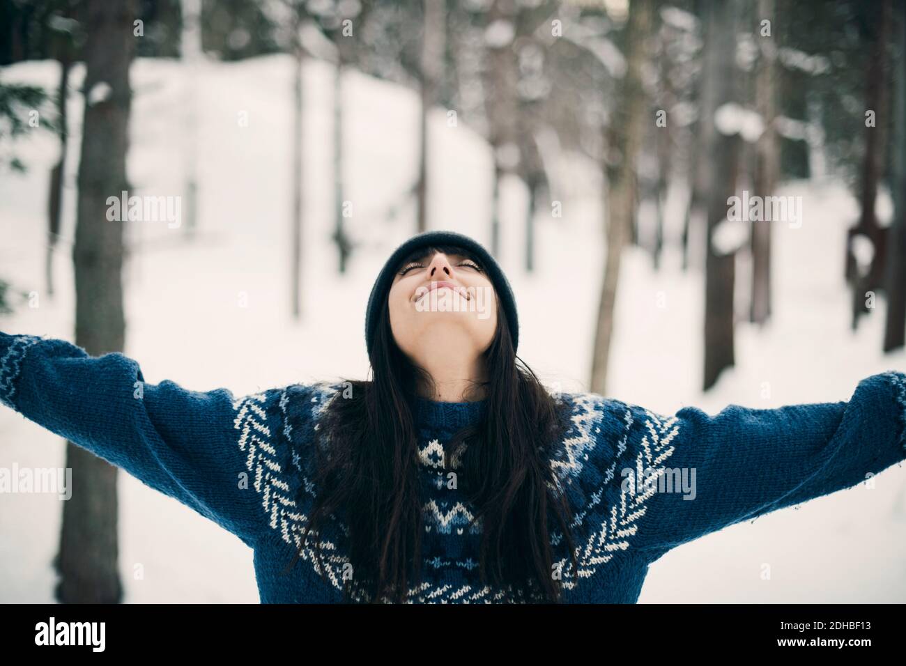 Happy woman standing with arms raised on snowy field during winter Stock Photo