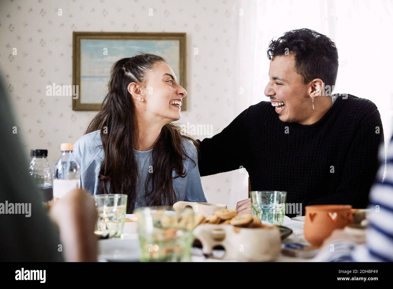 Cheerful friends looking at each other while sitting by food and drink in house Stock Photo