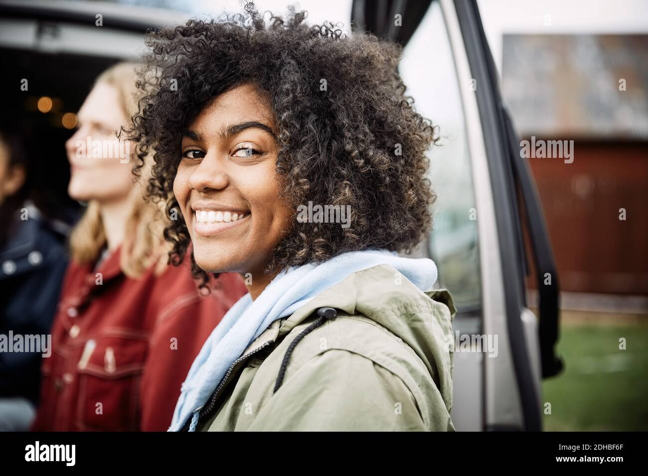 Portrait of smiling young woman with curly hair standing with friend by car Stock Photo