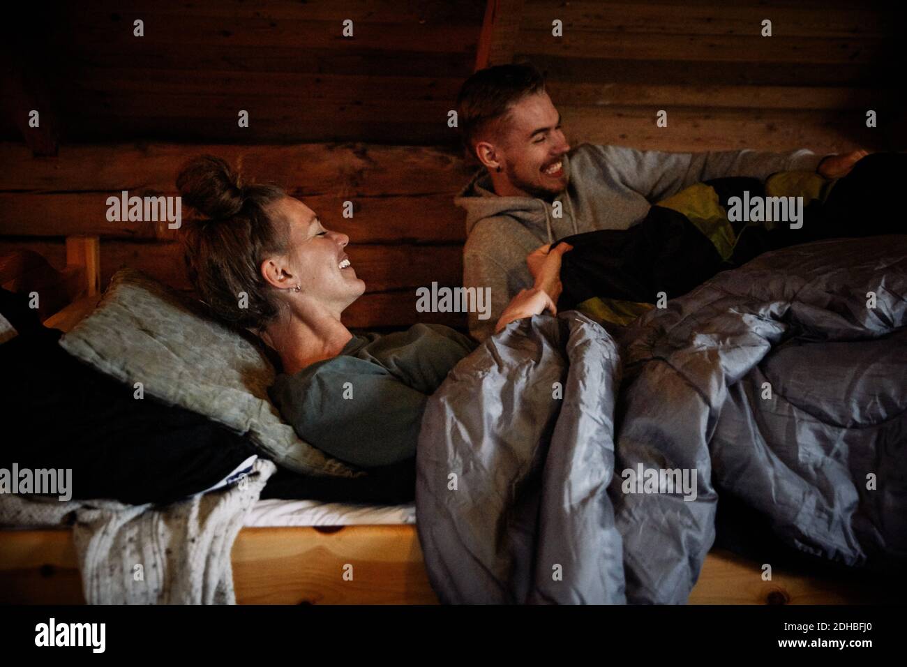 Smiling couple with blankets relaxing on bed in cottage Stock Photo