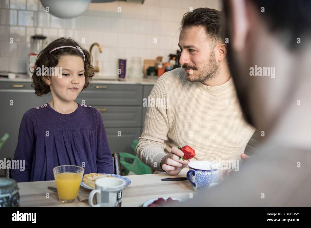 Father looking at daughter while having breakfast in kitchen Stock Photo