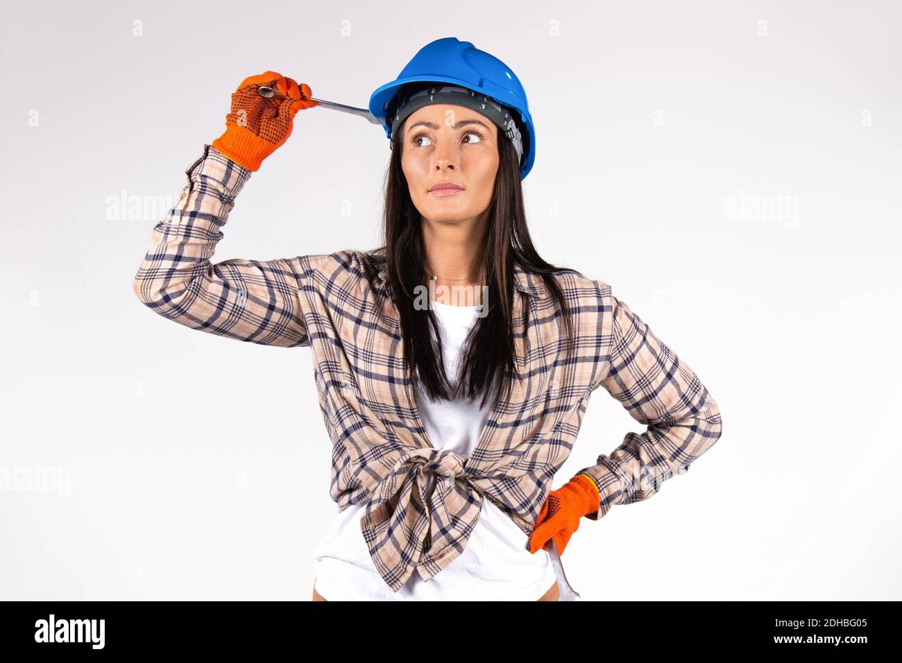 Female mechanic wearing blue hard hat holds a wrench and looks thoughtfully to the side. White background. Stock Photo